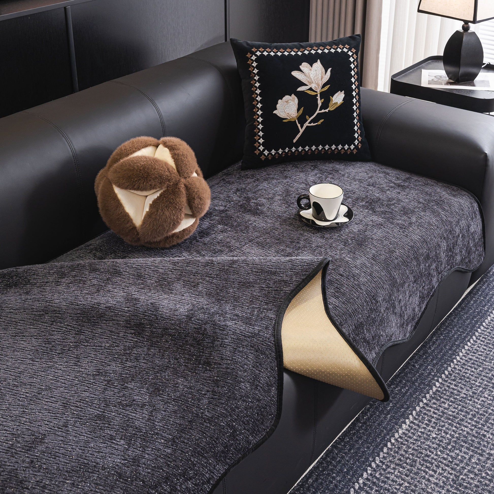 Chenille Couch Cover with Scalloped Edge, Non-Slip Modular Slipcover Sectional on a black leather sofa, enhancing elegance and comfort.