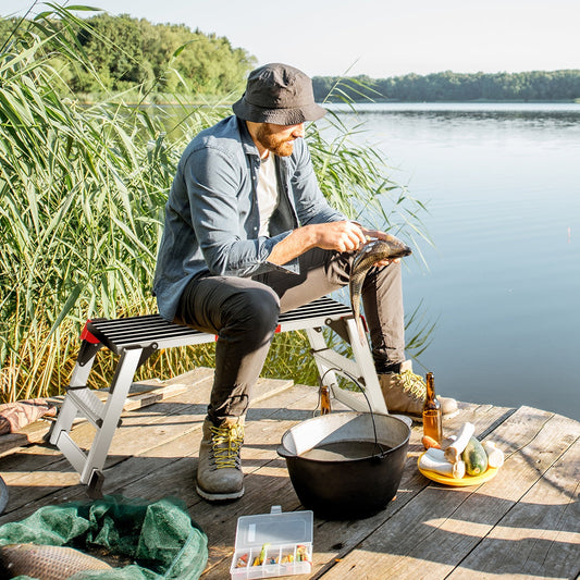 Man fishing on deck using 330 lbs Aluminum Folding Non-slip Drywall Step Stool Ladder, surrounded by fishing gear and nature.