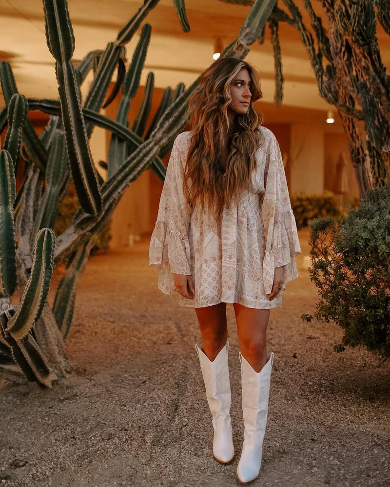 Woman in white dress wearing Embroidered Western Cowboy Knee-High Boots - Stylish Cowgirl Chic, standing among cacti at dusk.