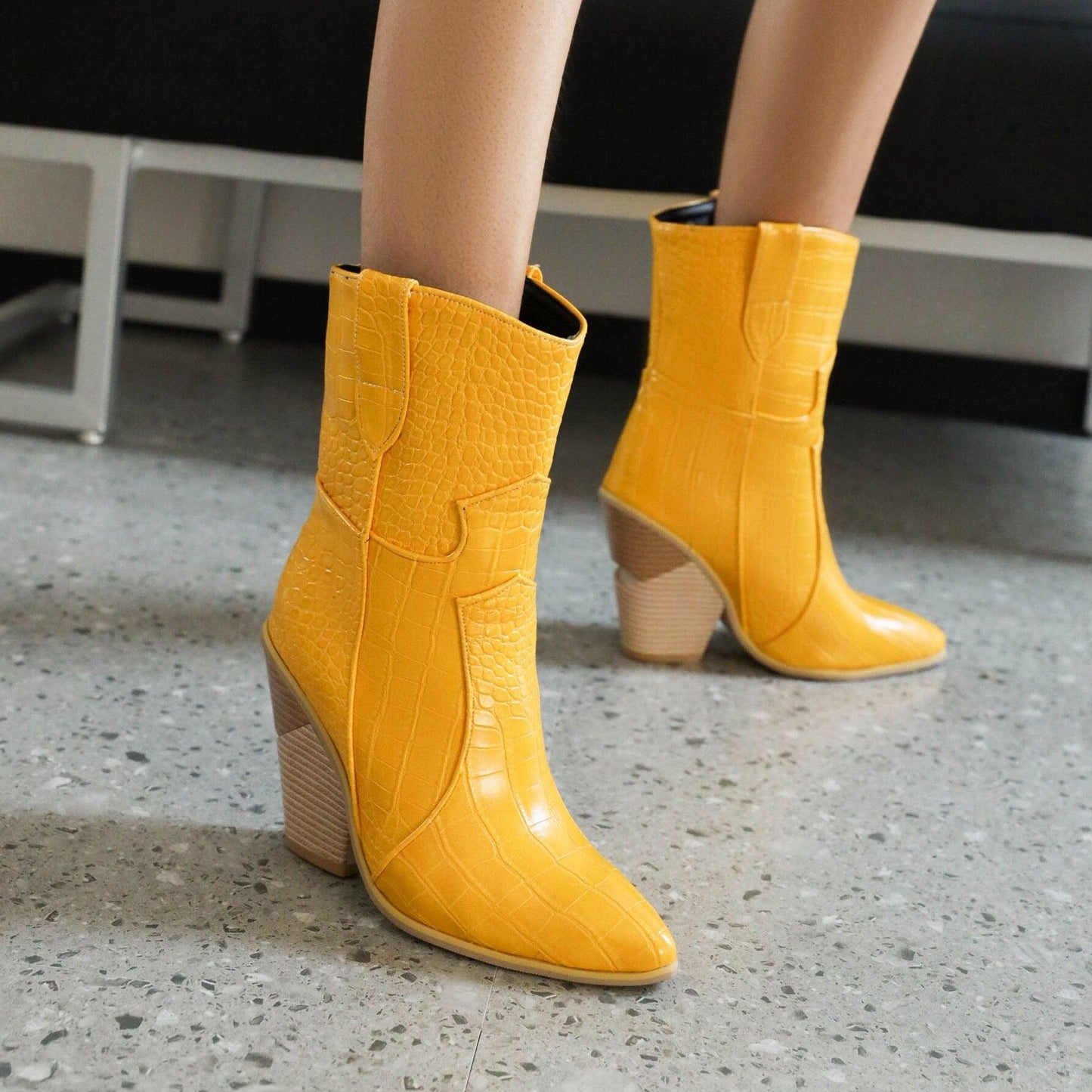 Yellow cowgirl chic high heel ankle boots with textured design on a stylish woman showcasing trendy denim and leather boots for women.