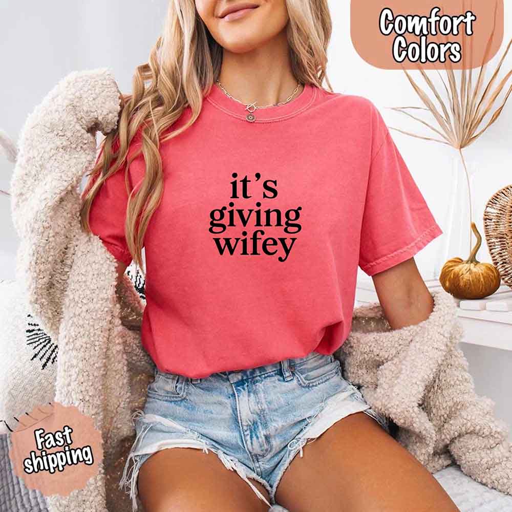 Model wearing Its Giving Wifey Comfort Colors Tee, perfect for brides, in a cozy room setting with decor. Fast shipping available.