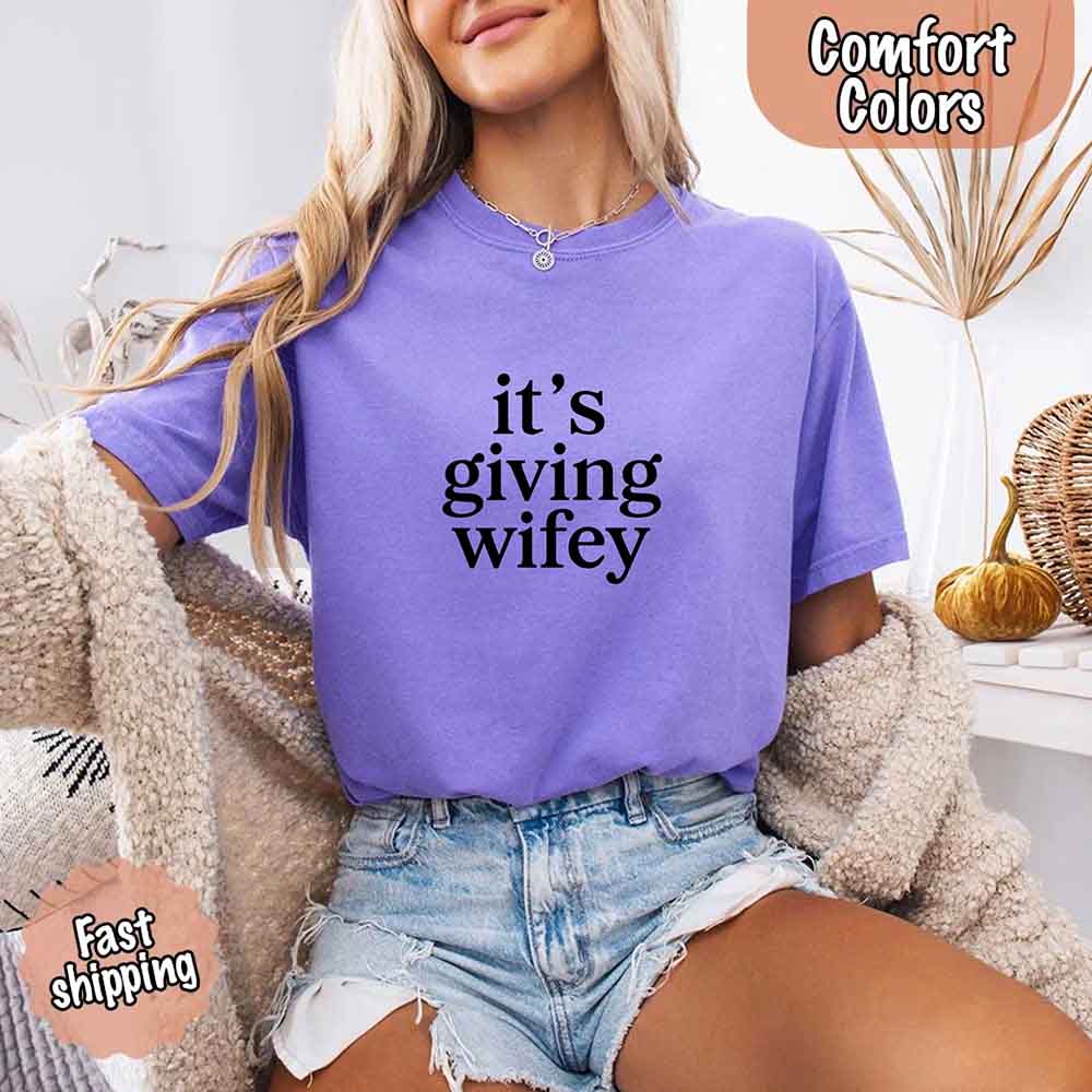 Woman wearing Its Giving Wifey Comfort Colors Tee, perfect bride gift shirt, showcasing chic bridal style in a cozy room setting.
