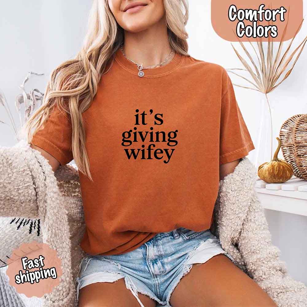 Woman wearing Its Giving Wifey Comfort Colors Tee in orange, styled with denim shorts, perfect for bride-to-be or wedding gift.