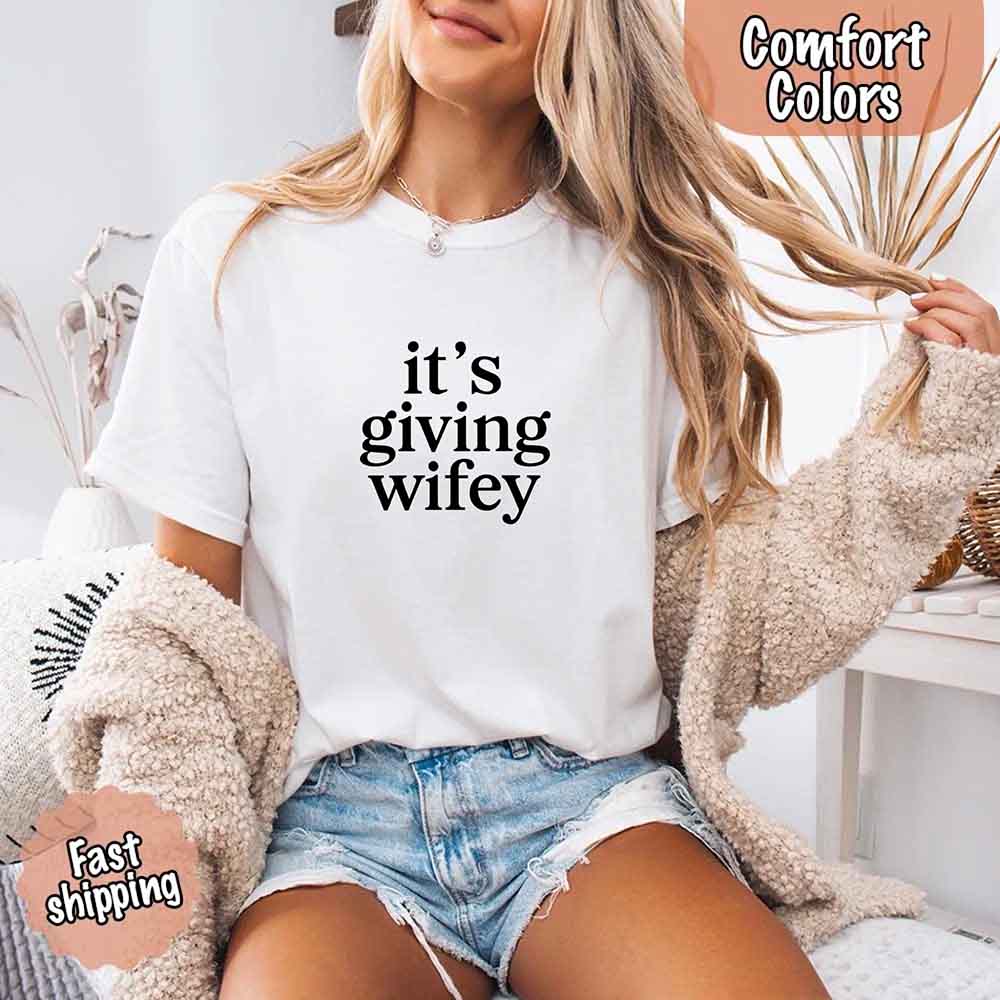 Woman wearing Its Giving Wifey Comfort Colors Tee, perfect for bridal occasions and honeymoon. Soft fabric, white tee with text print.