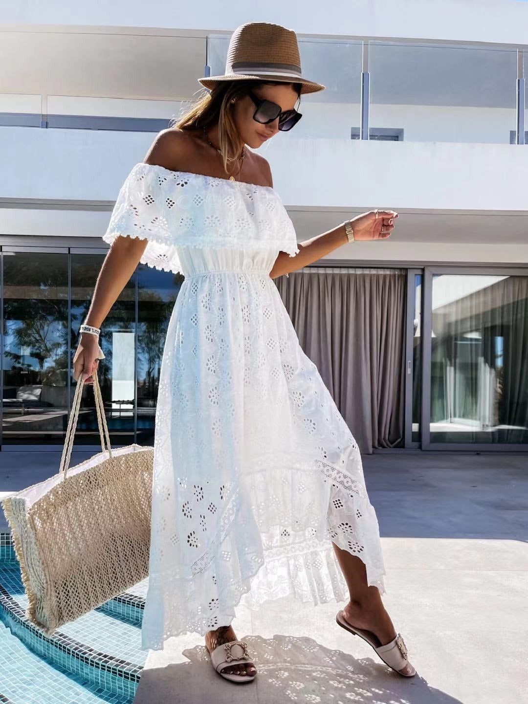 Woman wearing Bohemian Lace Princess Long Dress with off-shoulder design, holding a beach bag, walking by a modern building