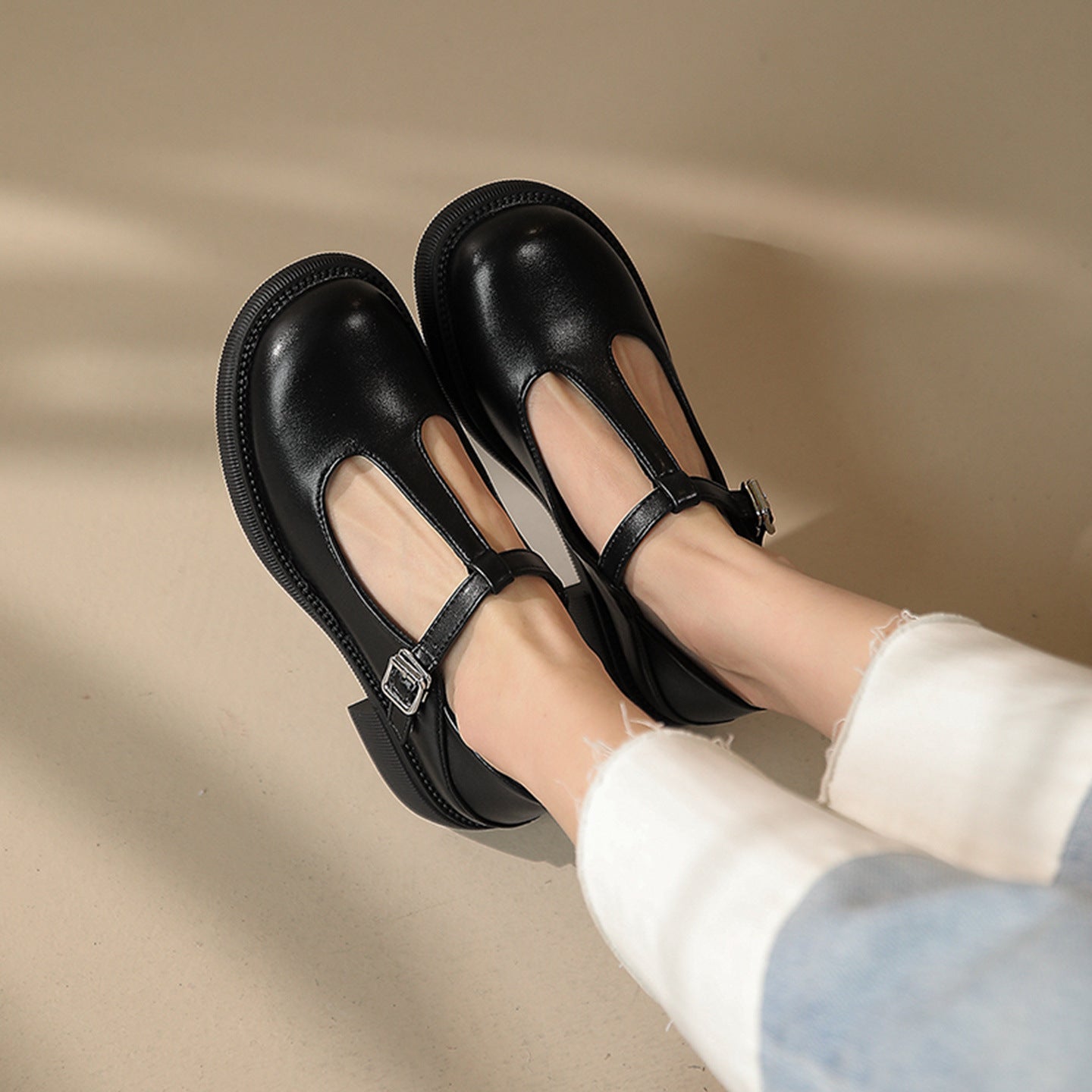 Women’s Shallow-Mouth Mary Jane Shoes in black with classic strap and retro design on beige background, flat heel, stylish footwear.