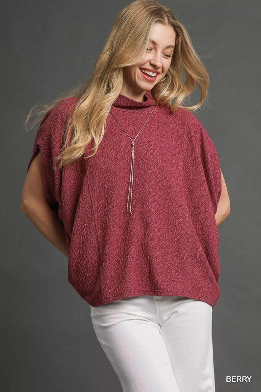 Woman wearing Umgee Textured Mock Neck Relaxed Top in berry color with short dolman sleeves and straight hemline.