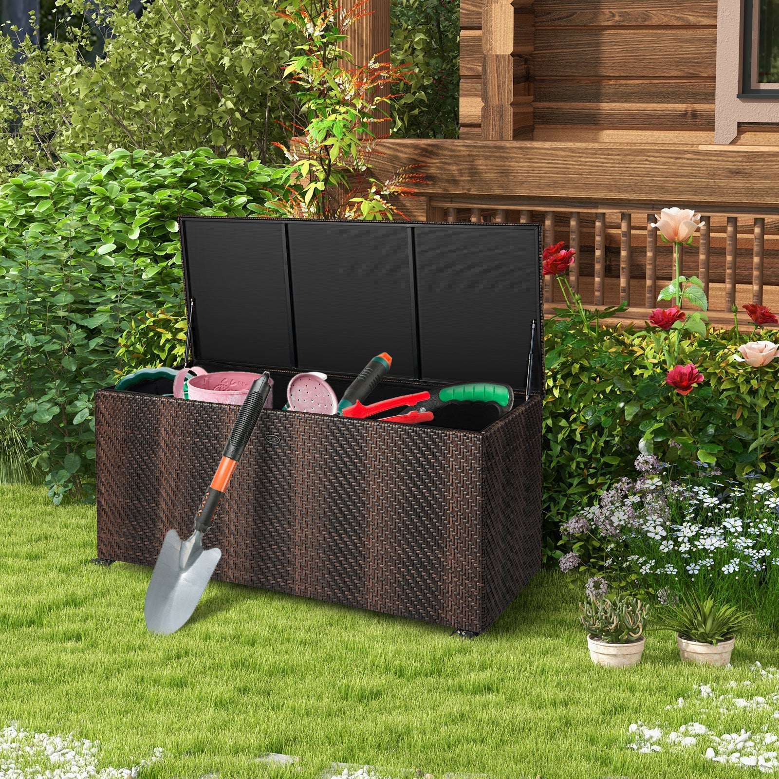 96 Gallon PE Wicker Outdoor Storage Box with 4 Wheels-Brown in a garden setting, open with gardening tools inside