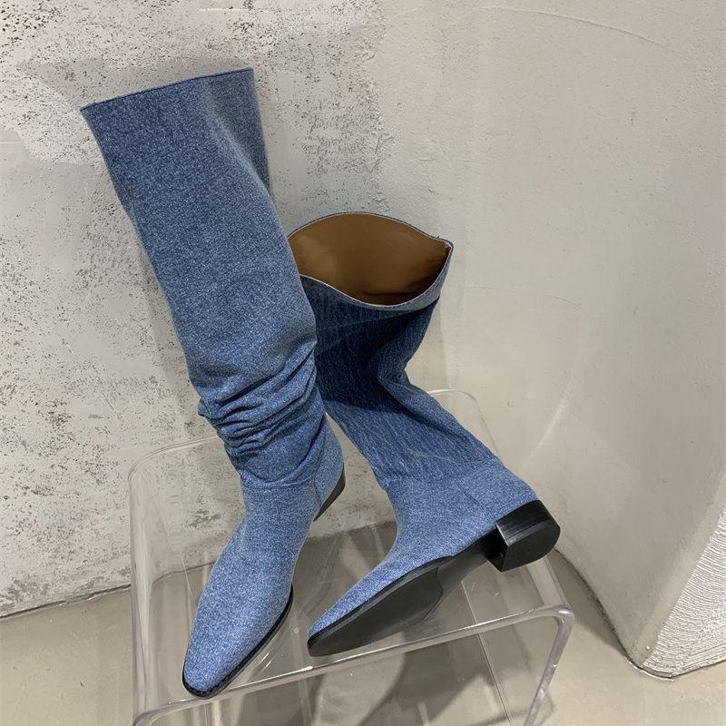Women’s Denim Knee High Boots - Casual Cowboy Style displayed against a textured wall, showcasing their unique design and low heel.