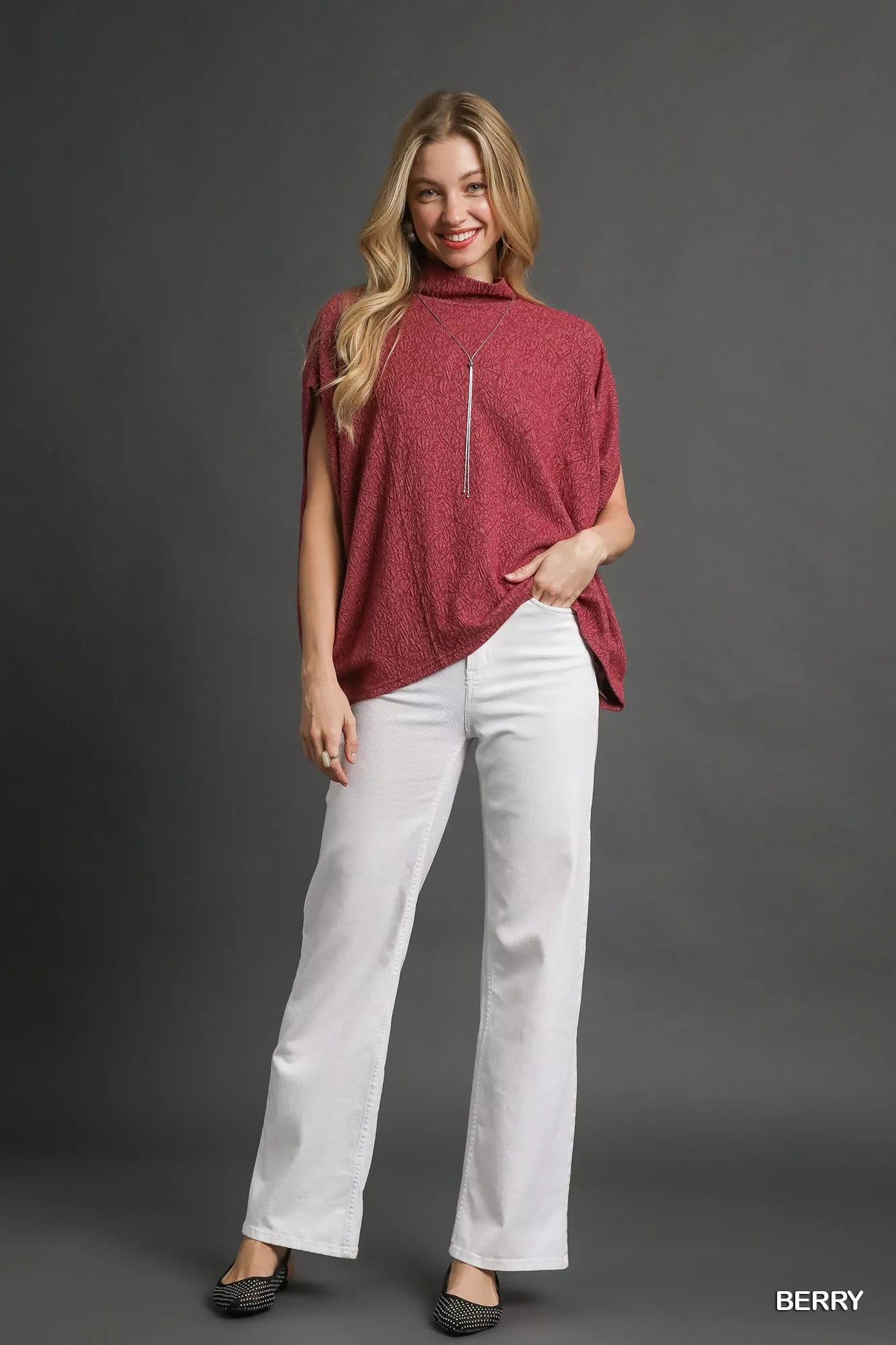 Woman wearing Umgee Textured Mock Neck Relaxed Top in berry with white pants and black shoes