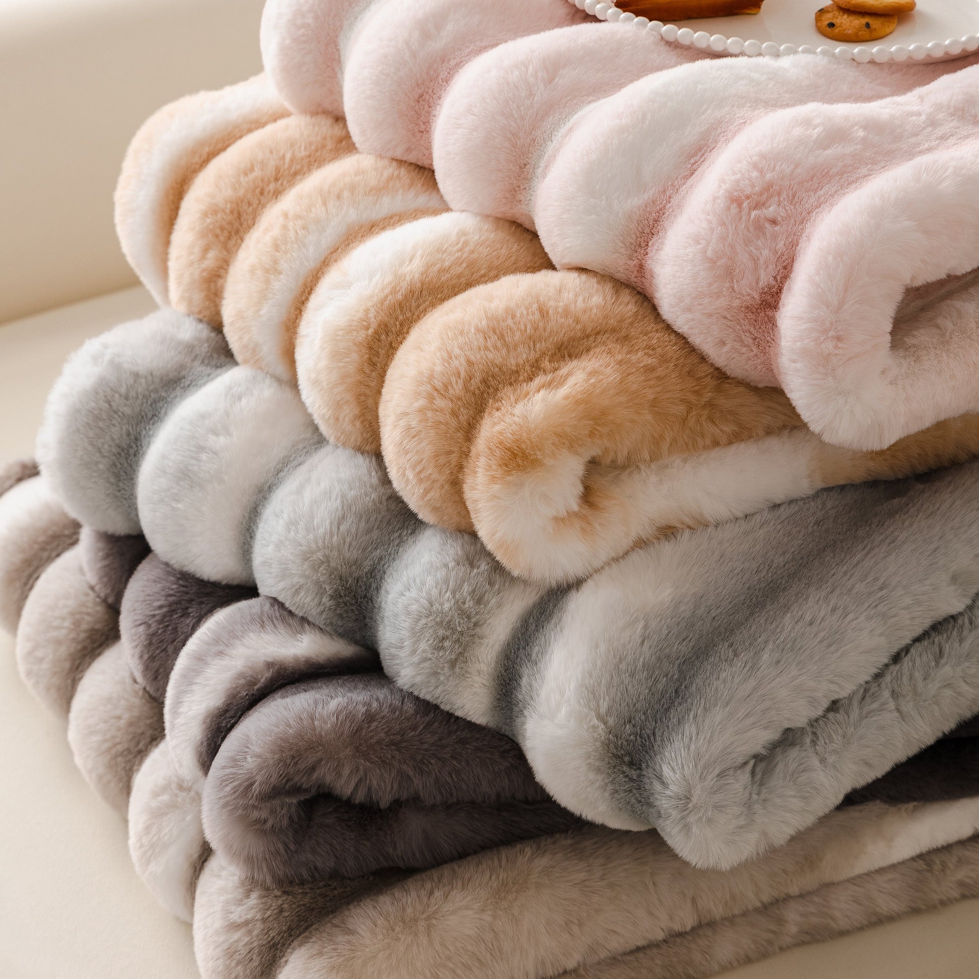 Stack of pastel Ultra Soft Faux Fur Couch Cover – Large, Fluffy, and Elegant Sofa Throw Blanket in gradient colors on a sofa