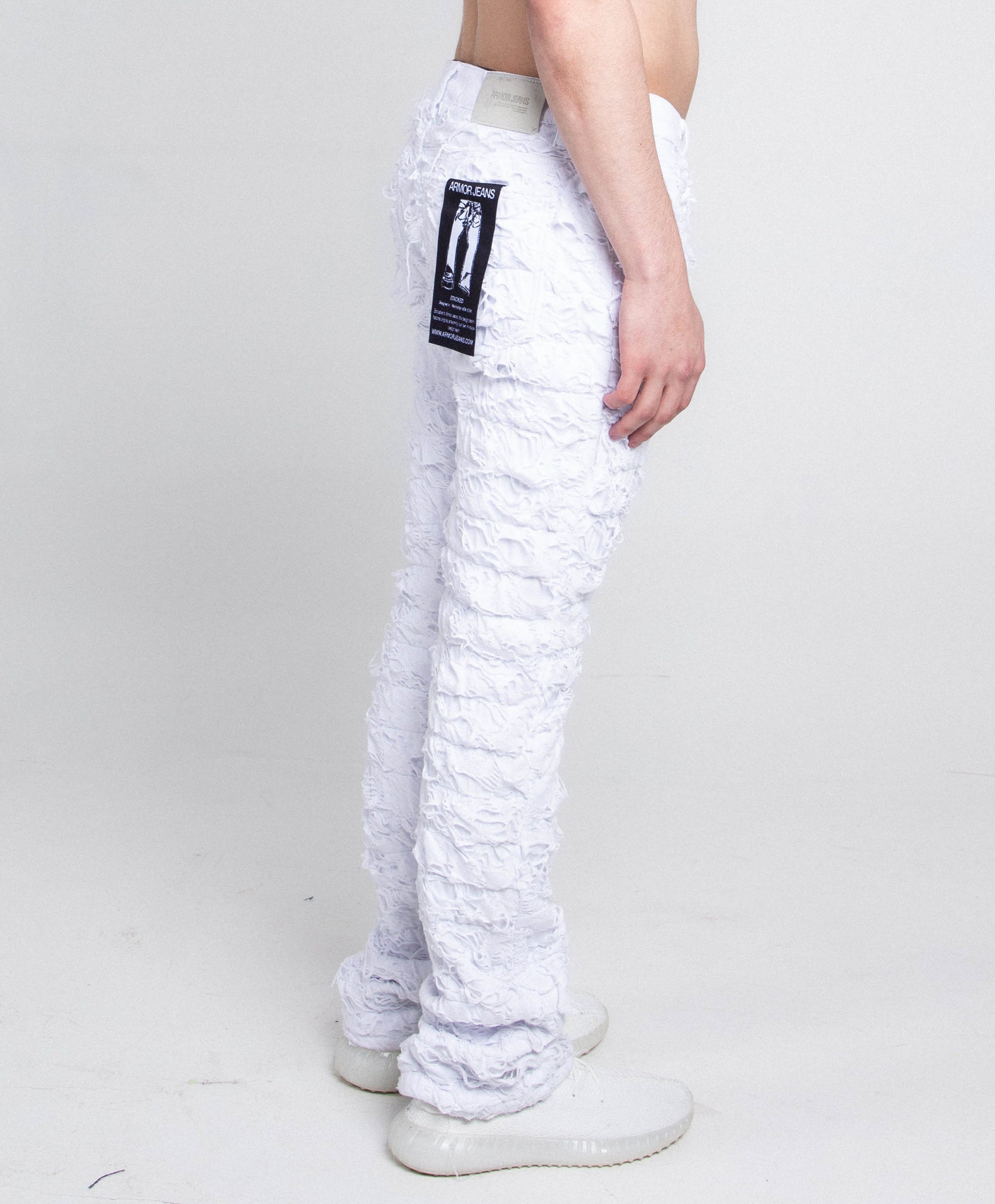 Side view of AR704 WHITE FRAYED STACKED JEANS showcasing frayed detailing and mid-rise stretchy fit with zipper fly and button fastening.