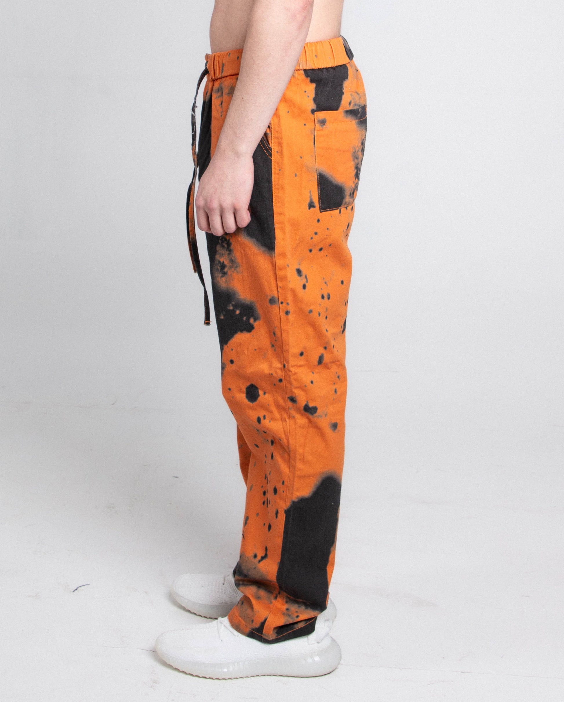 Side view of AJ04L COLOR DYE LOOSE JEANS with black dye detail, five-pocket design, and elastic band fastening in orange.
