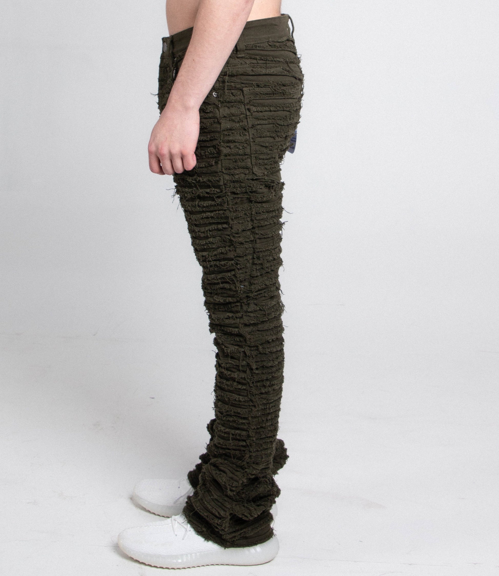 Side view of AJS693 EXTREME FRAYED STACKED JEANS showcasing mid rise and frayed inseam with stacked leg design, worn with white shoes.