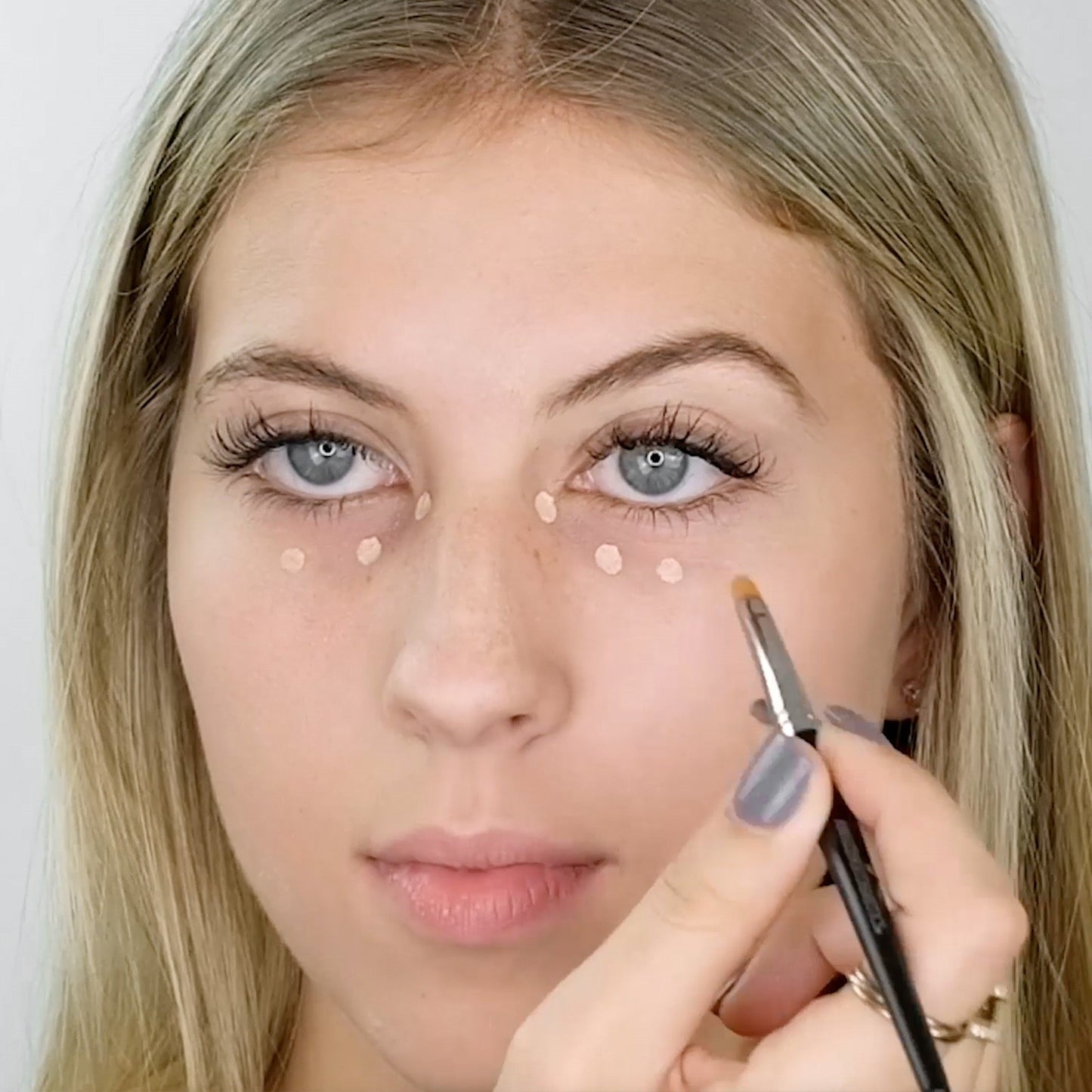 Woman applying concealer with a Concealer Brush for precise coverage under the eyes, targeting blemishes with expert precision.