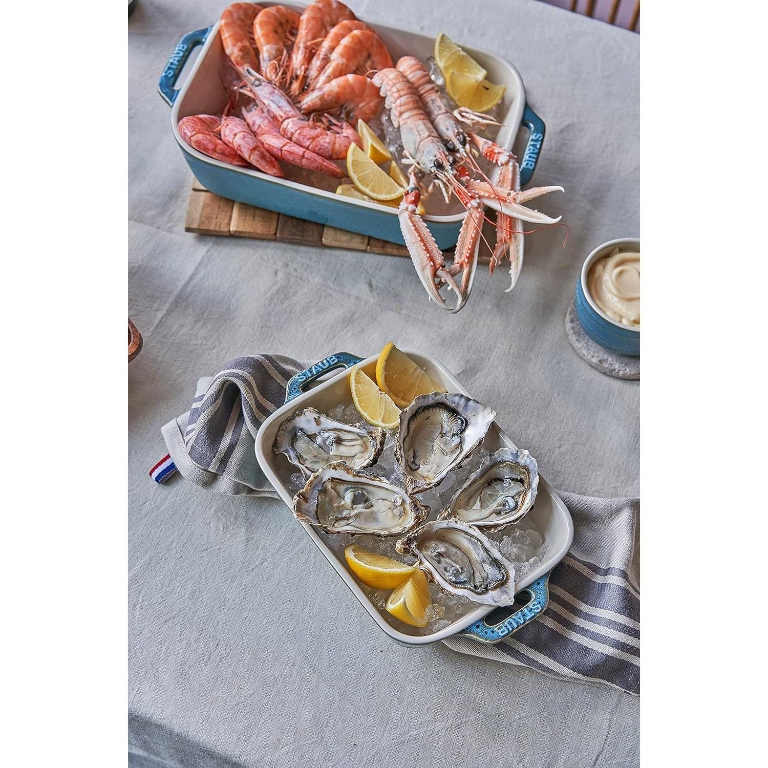 Set of 2 - Ceramic Stoneware Baking Dish Set in Blue Green Turquoise Ivory with seafood and lemon slices on a table.