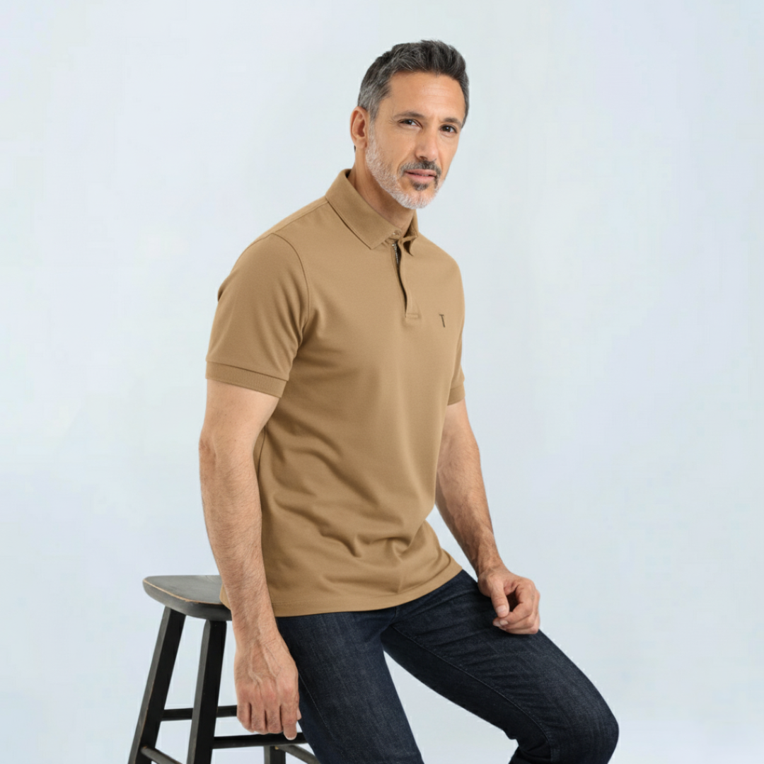 Man wearing tan Short Sleeve Perfect Polo with StaySharp™ Collar, sitting on stool. Stylish, wrinkle-free, modern fit polo for everyday use.