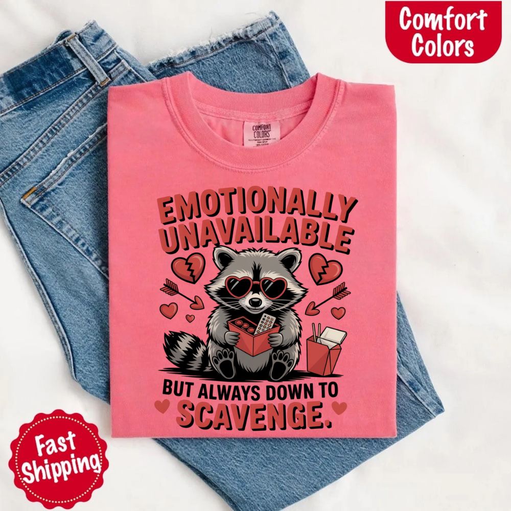 Comfort Colors Emotionally Unavailable Raccoon T-Shirts, pink with moody raccoon print, displayed on denim.
