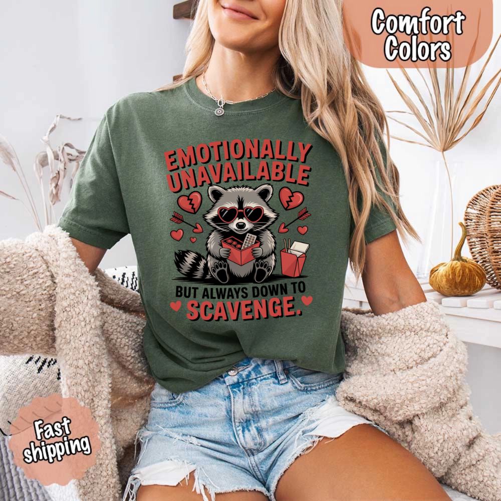 Person wearing Comfort Colors Emotionally Unavailable Raccoon T-Shirts with moody raccoon graphic, fast shipping badge visible.