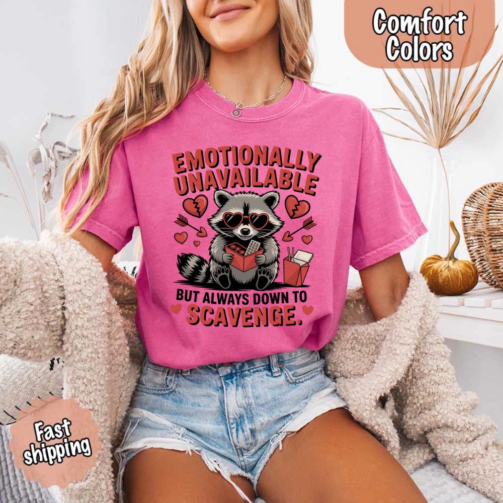 Woman wearing pink Comfort Colors Emotionally Unavailable Raccoon T-Shirt with moody raccoon graphic.