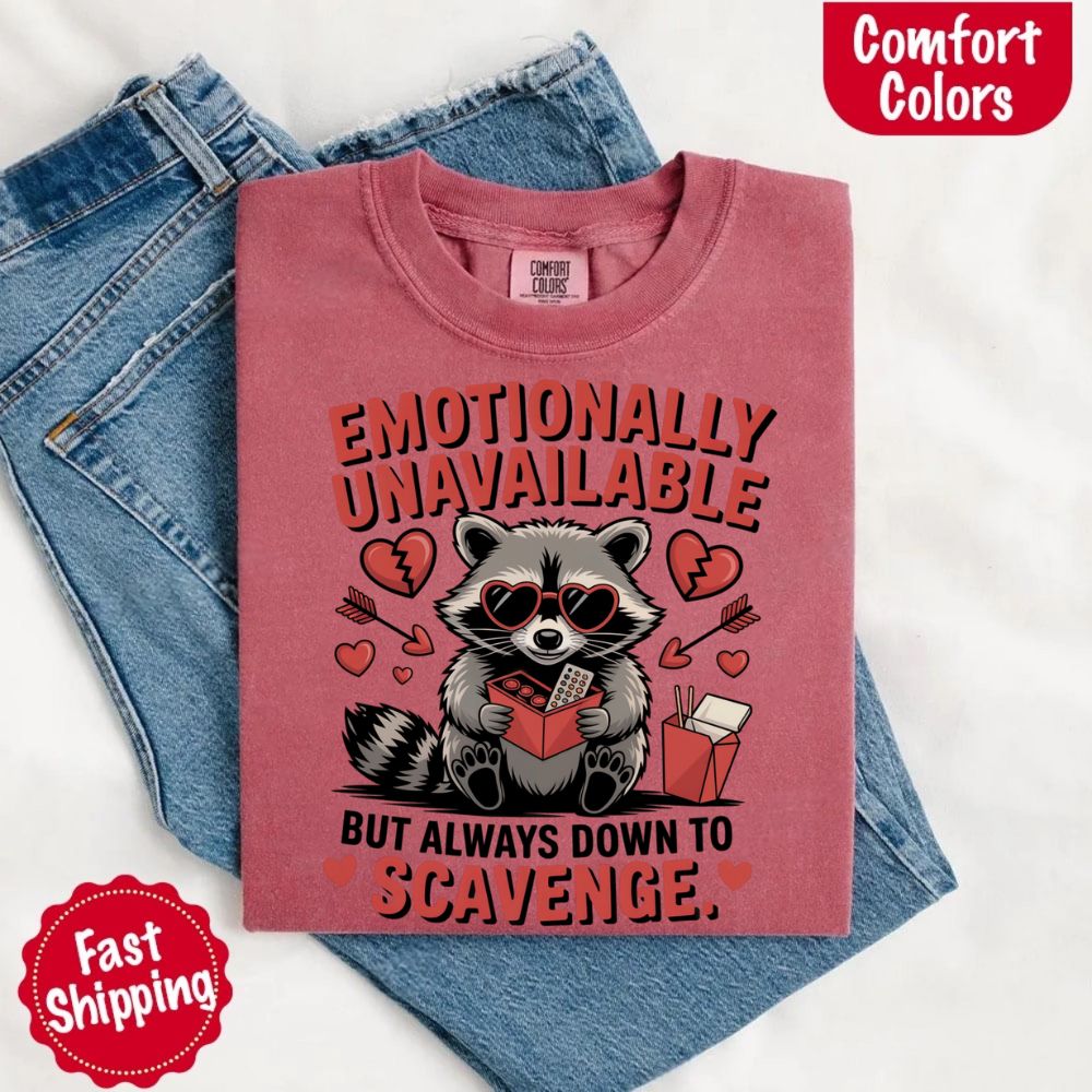Comfort Colors Emotionally Unavailable Raccoon T-Shirts with moody raccoon graphic on pink tee, fast shipping label, and jeans background.