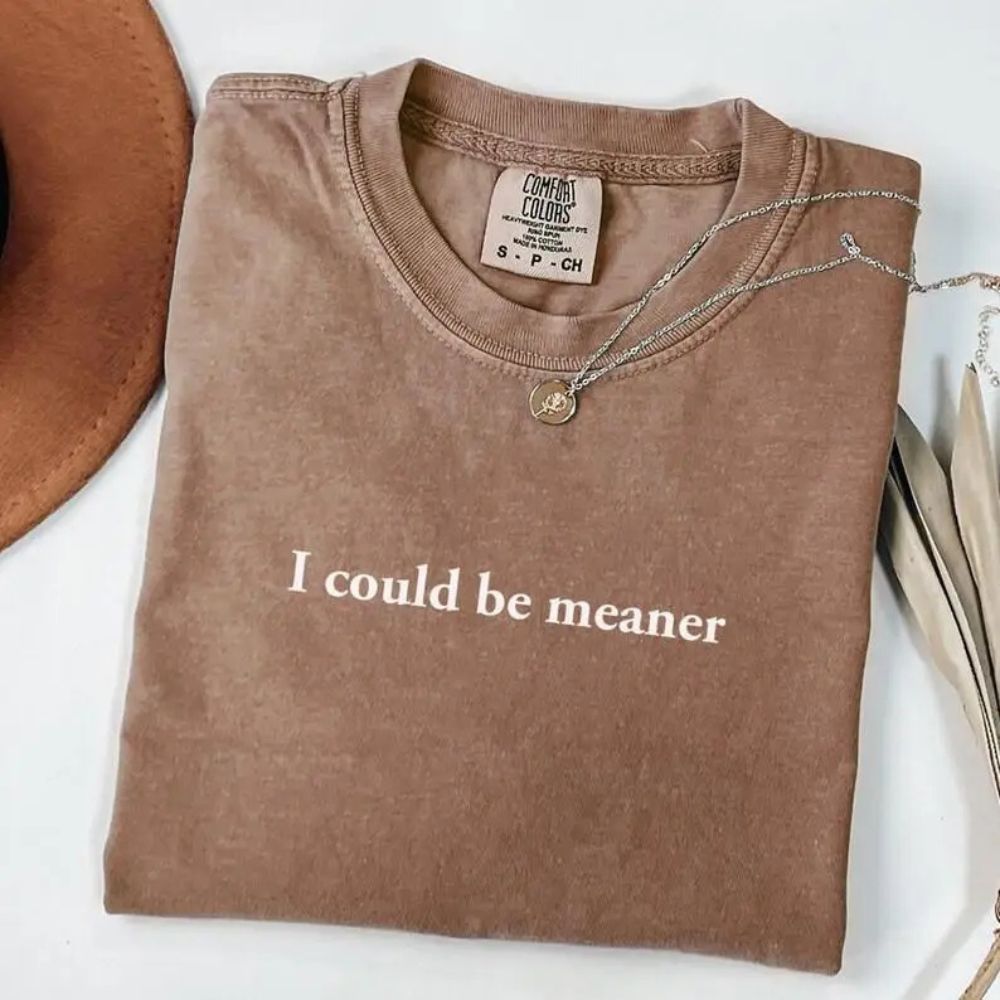 I Could Be Meaner Funny Sarcastic Tee folded with necklace, trendy streetwear fashion.