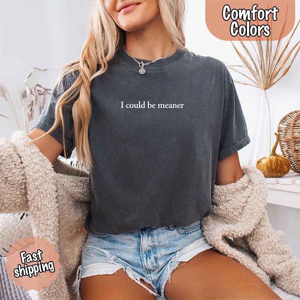 Woman wearing 'I Could Be Meaner Funny Sarcastic Tee' with comfort colors, denim shorts, sitting stylishly with a cozy vibe.