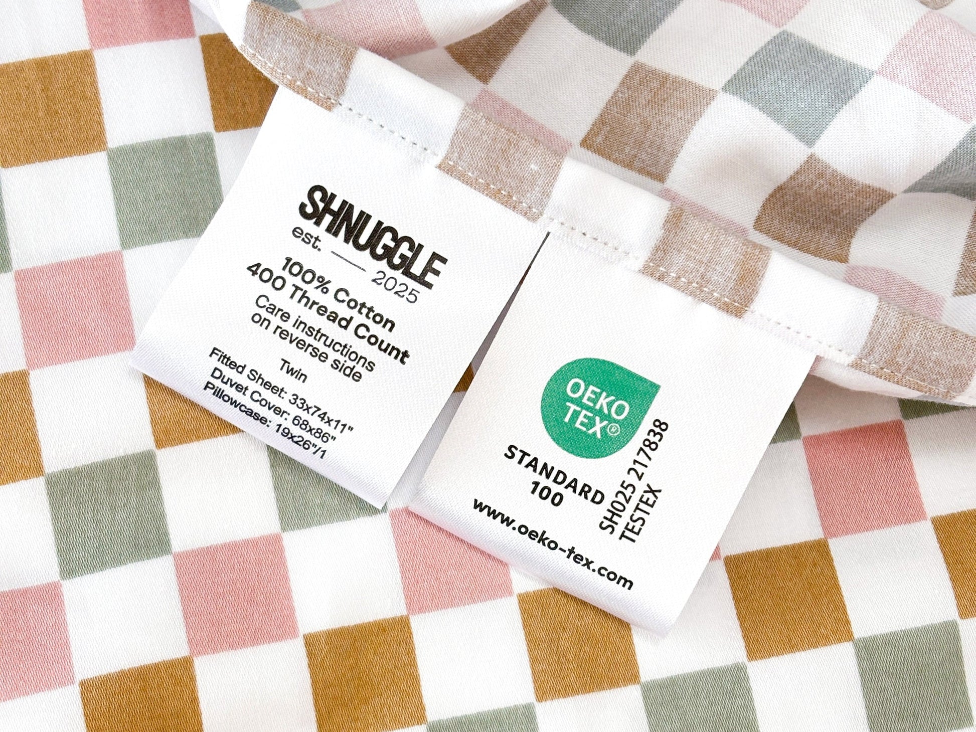 Fitted Sheet 28"x63"- SHNUGGLE with colorful checkered pattern and care instructions tag visible.