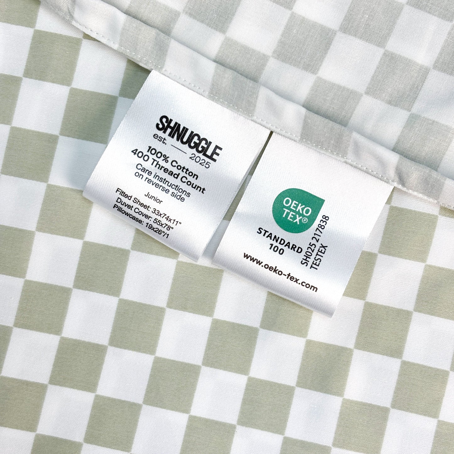 Close-up of SHNUGGLE Bedding Set Sage Checker fabric with care labels