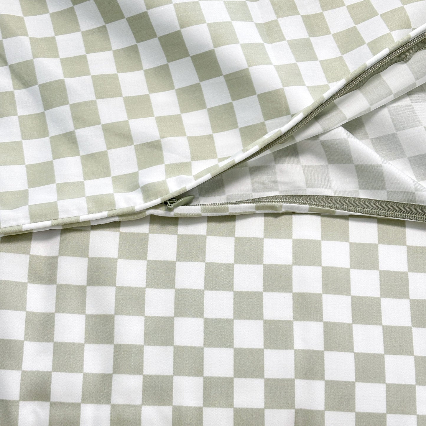 Close-up of SHNUGGLE Bedding Set Sage Checker showing zipper detail on checkered fabric.