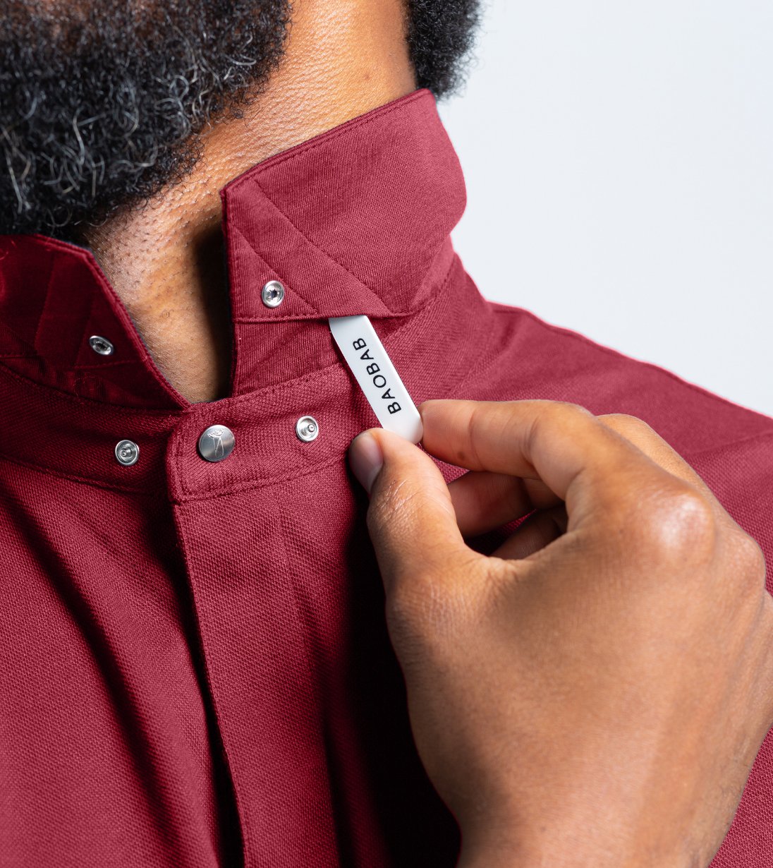 Man adjusting StaySharp™ Collar on Baobab Short Sleeve Perfect Polo, showcasing modern innovation and tailored comfort in red color.