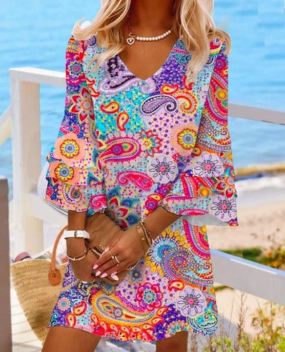 Woman wearing Classic V-Neck Beach Dress with vibrant floral pattern in rose, blue, and gray, featuring 3/4 sleeves by the sea.