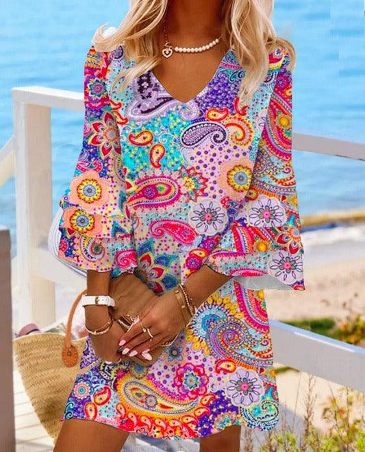 Woman wearing Classic V-Neck Beach Dress with vibrant floral pattern in rose, blue, and gray, featuring 3/4 sleeves by the sea.