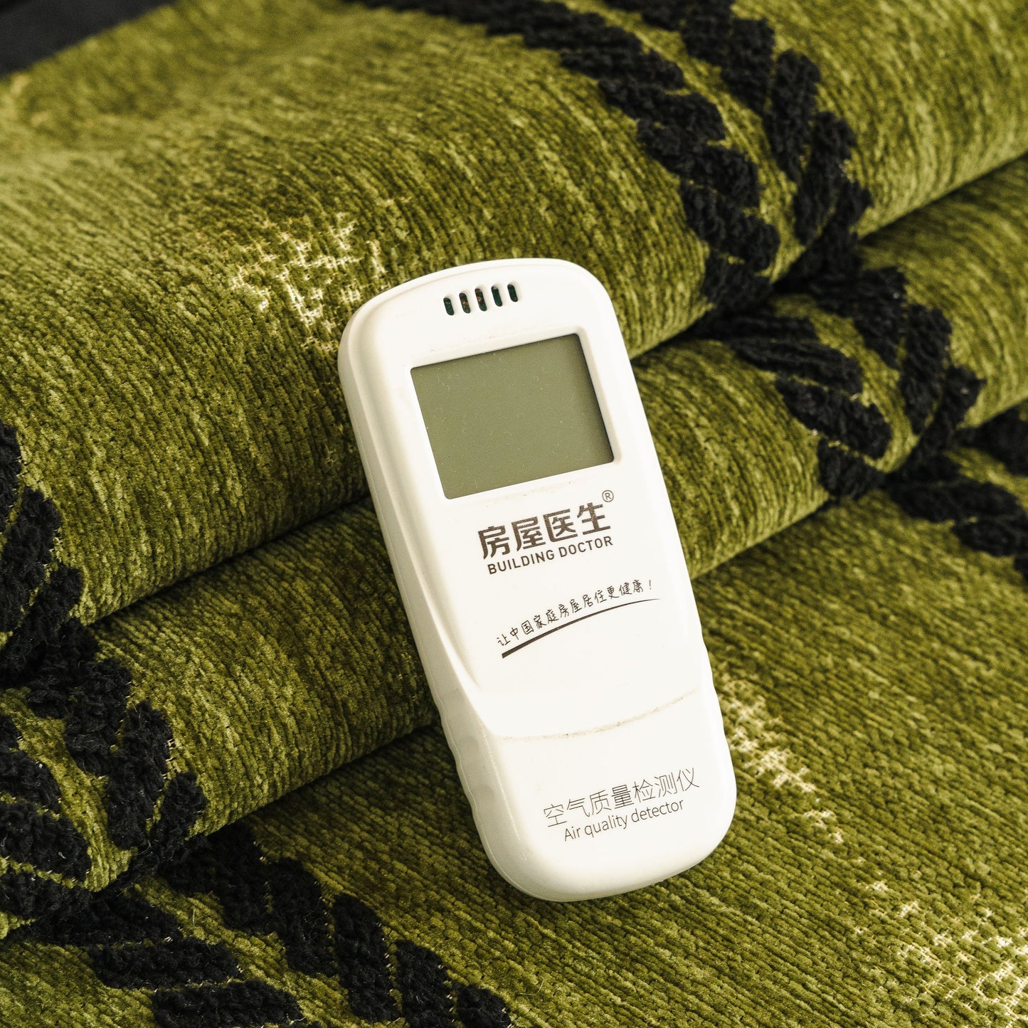 Air quality detector on green chenille fabric with woven texture pattern.