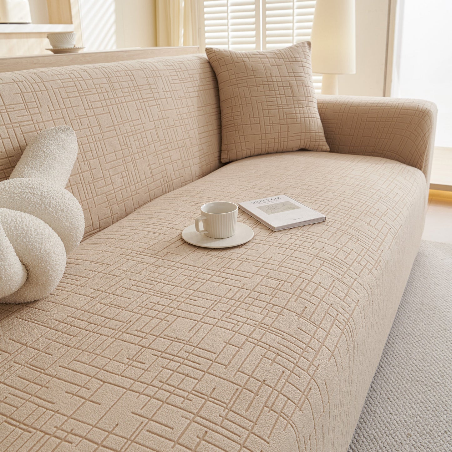 Beige Embossed Lines Couch Covers Stretchable Non-Slip & Washable Sofa Slipcovers on a sofa with a cushion and cup of coffee.
