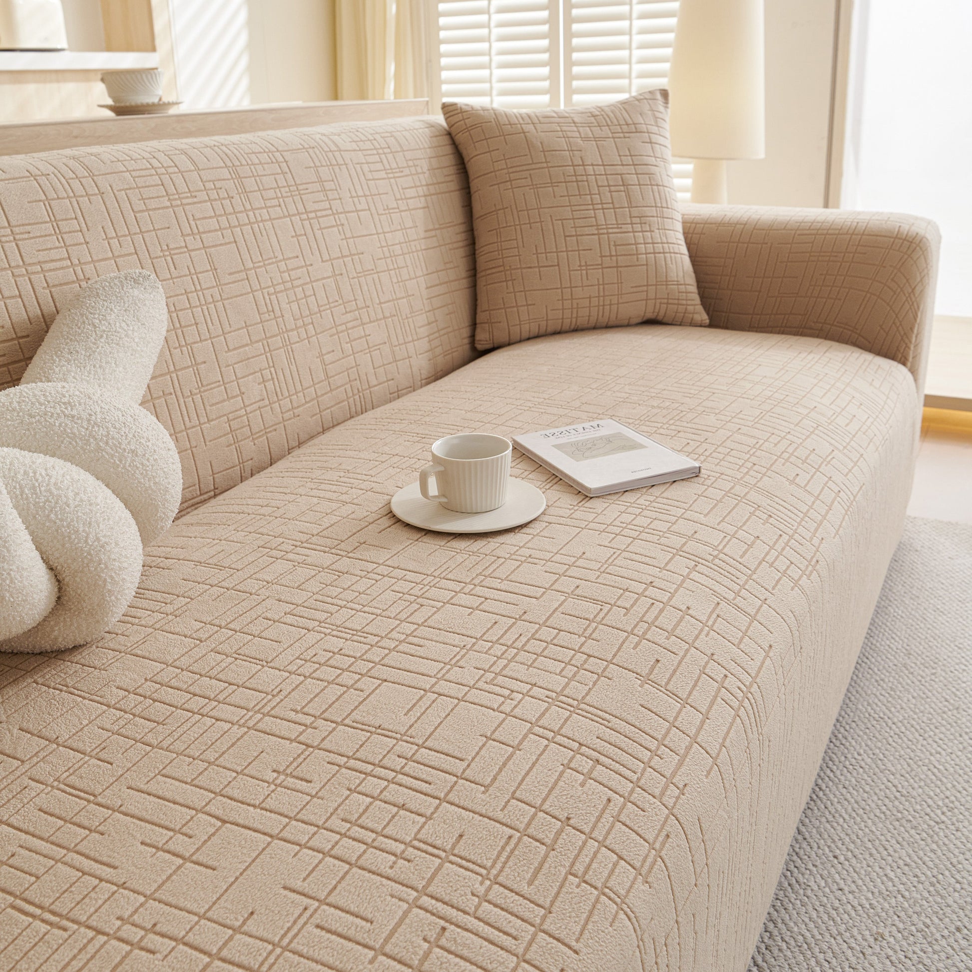 Beige Embossed Lines Couch Covers Stretchable Non-Slip & Washable Sofa Slipcovers on a sofa with a cushion and cup of coffee.