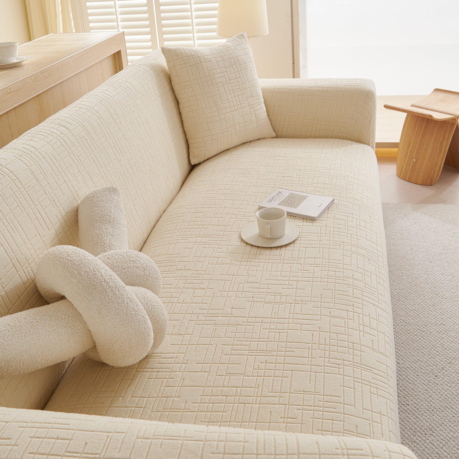 Embossed Lines Couch Covers Stretchable Non-Slip & Washable Sofa Slipcovers on a cream sofa with a cushion and decorative knot pillow.