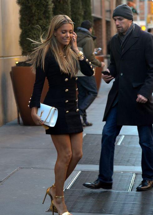 Woman wearing Sophisticated Black Gold Button Dress walking down the street, holding a white clutch, showcasing a chic, formal style.