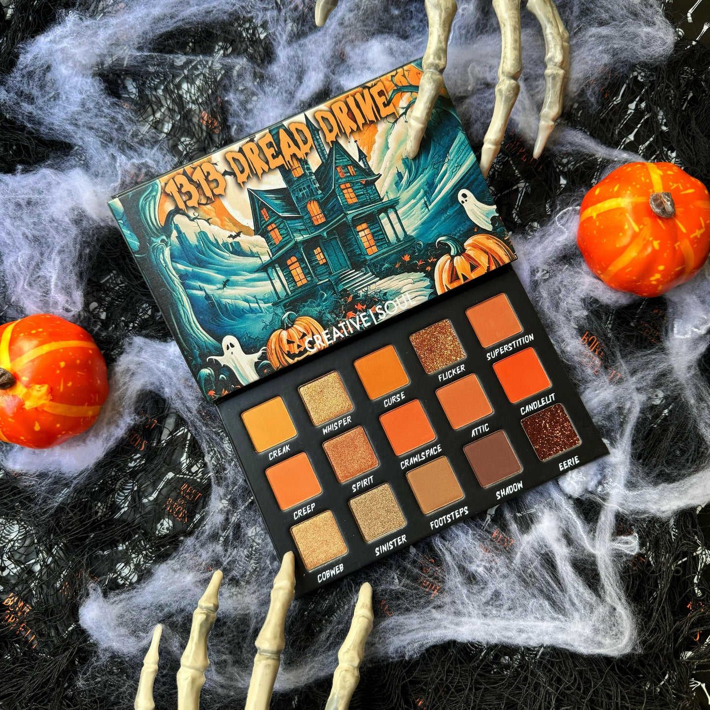 1313 Dread Drive Eyeshadow Palette with haunted house and Halloween-themed colors, displayed with pumpkins and skeleton decor.