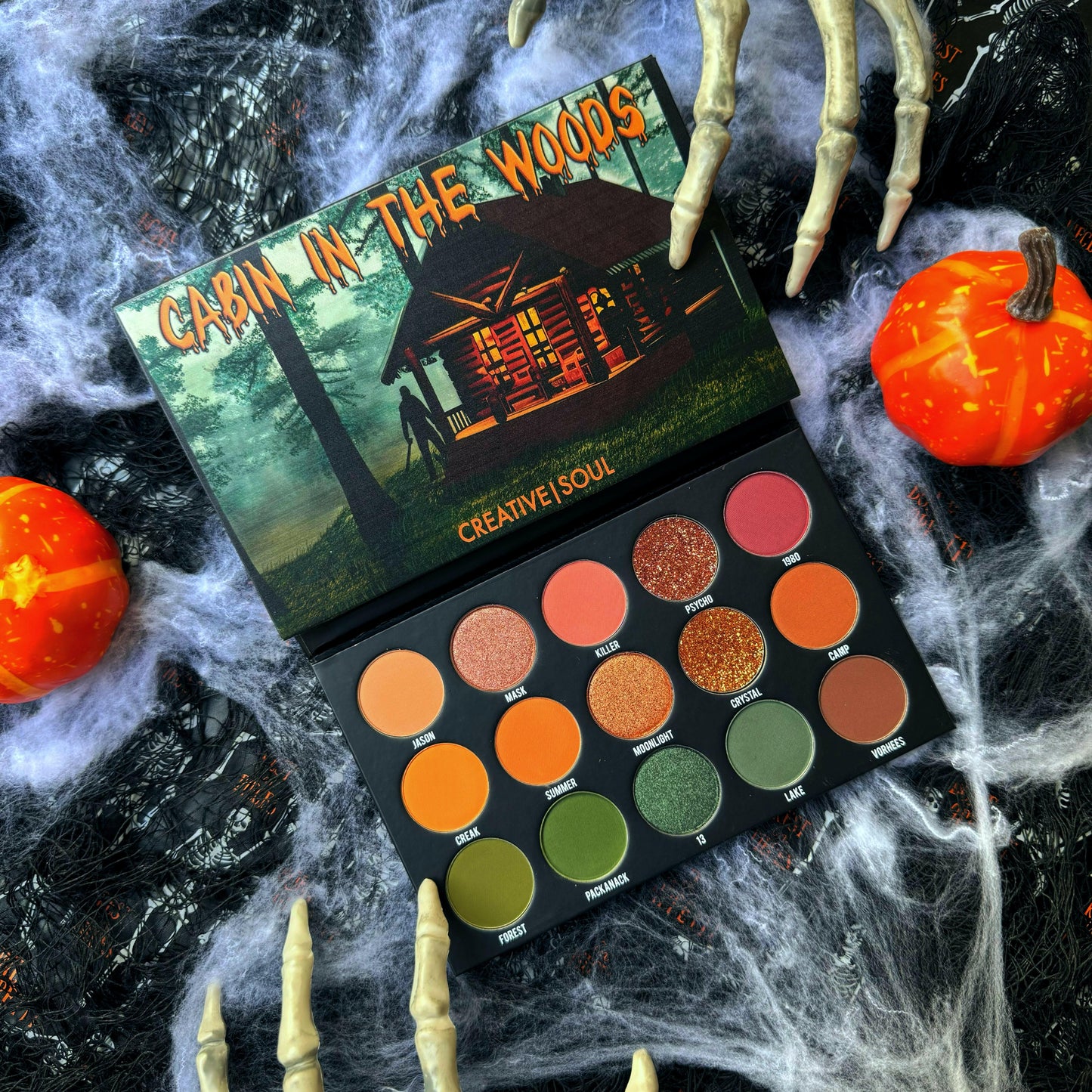 Cabin In The Woods Eyeshadow Palette with 80s slasher film-inspired shades, surrounded by Halloween decorations and cobwebs.