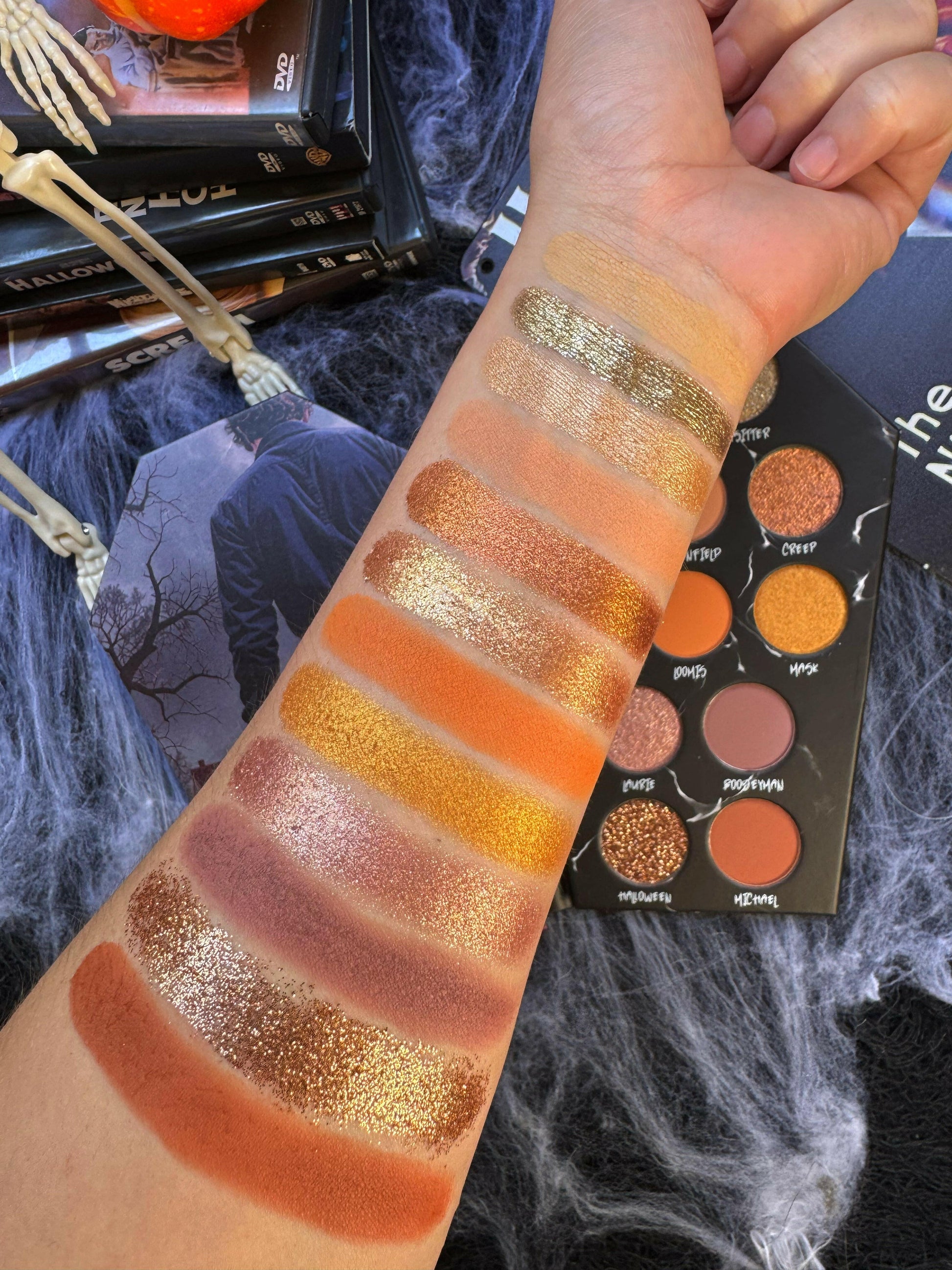 Swatches of Stalker Eyeshadow Palette featuring neutral shades on arm, makeup display, Halloween theme.