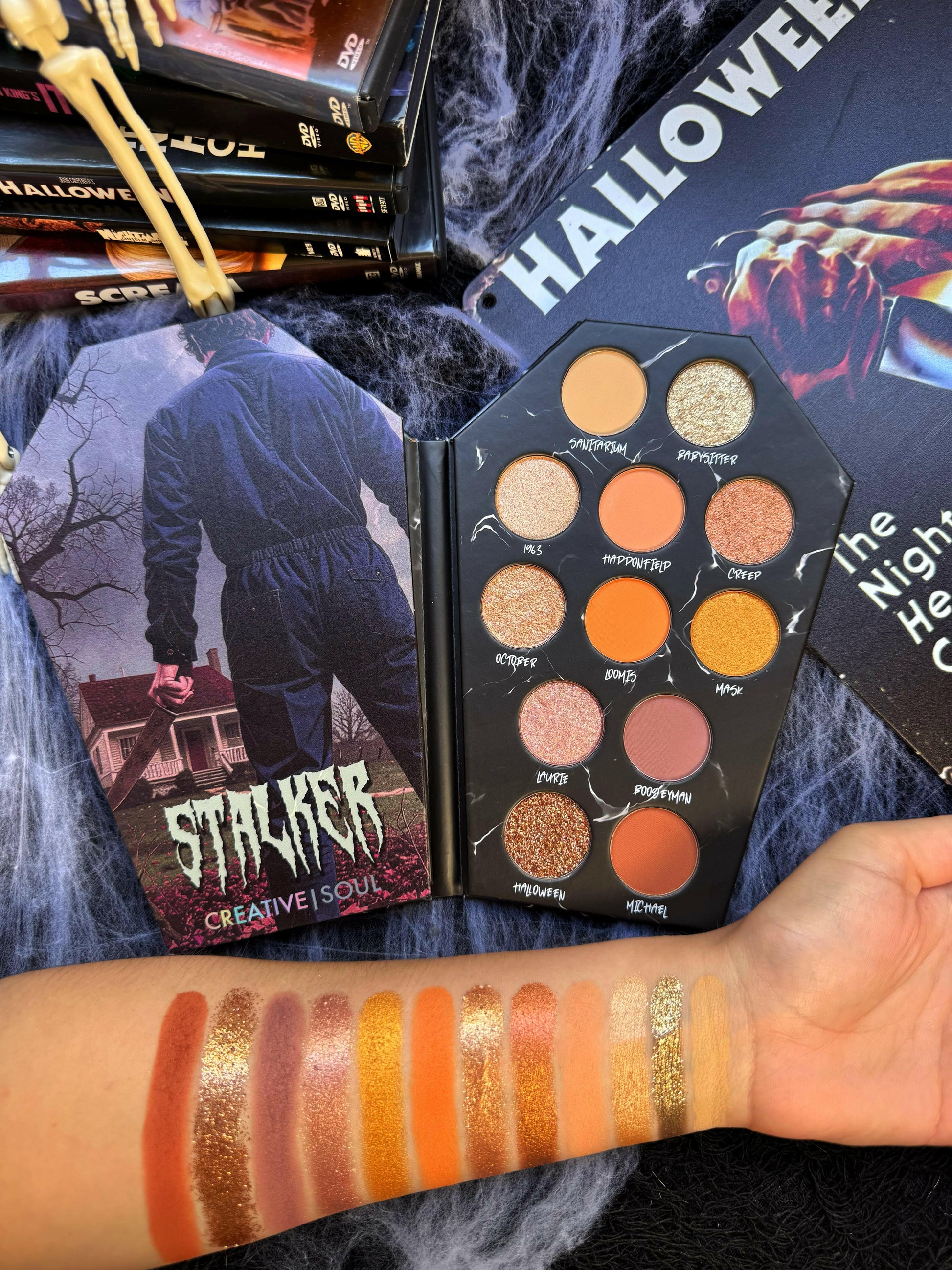 Open Stalker Eyeshadow Palette featuring neutral shades with arm swatches, surrounded by Halloween-themed decor.