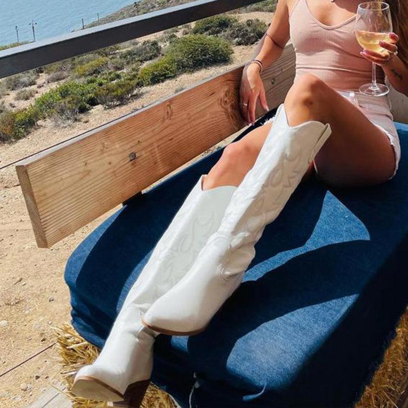 Woman relaxing in Embroidered Western Cowboy Knee-High Boots - Stylish Cowgirl Chic, enjoying a scenic view with a glass of wine.
