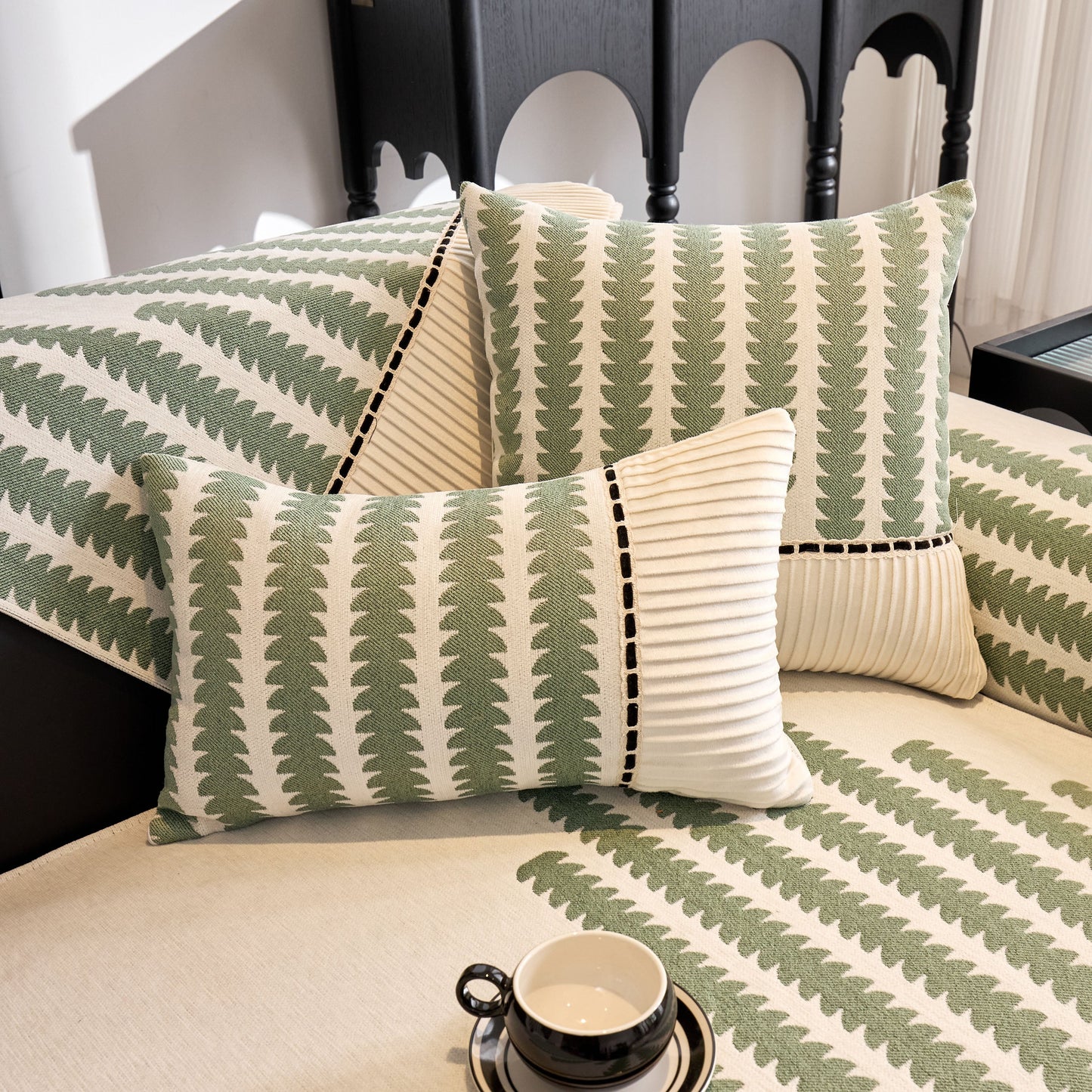 Green and white patterned pillows and cushion on a sofa with a cup on the table.