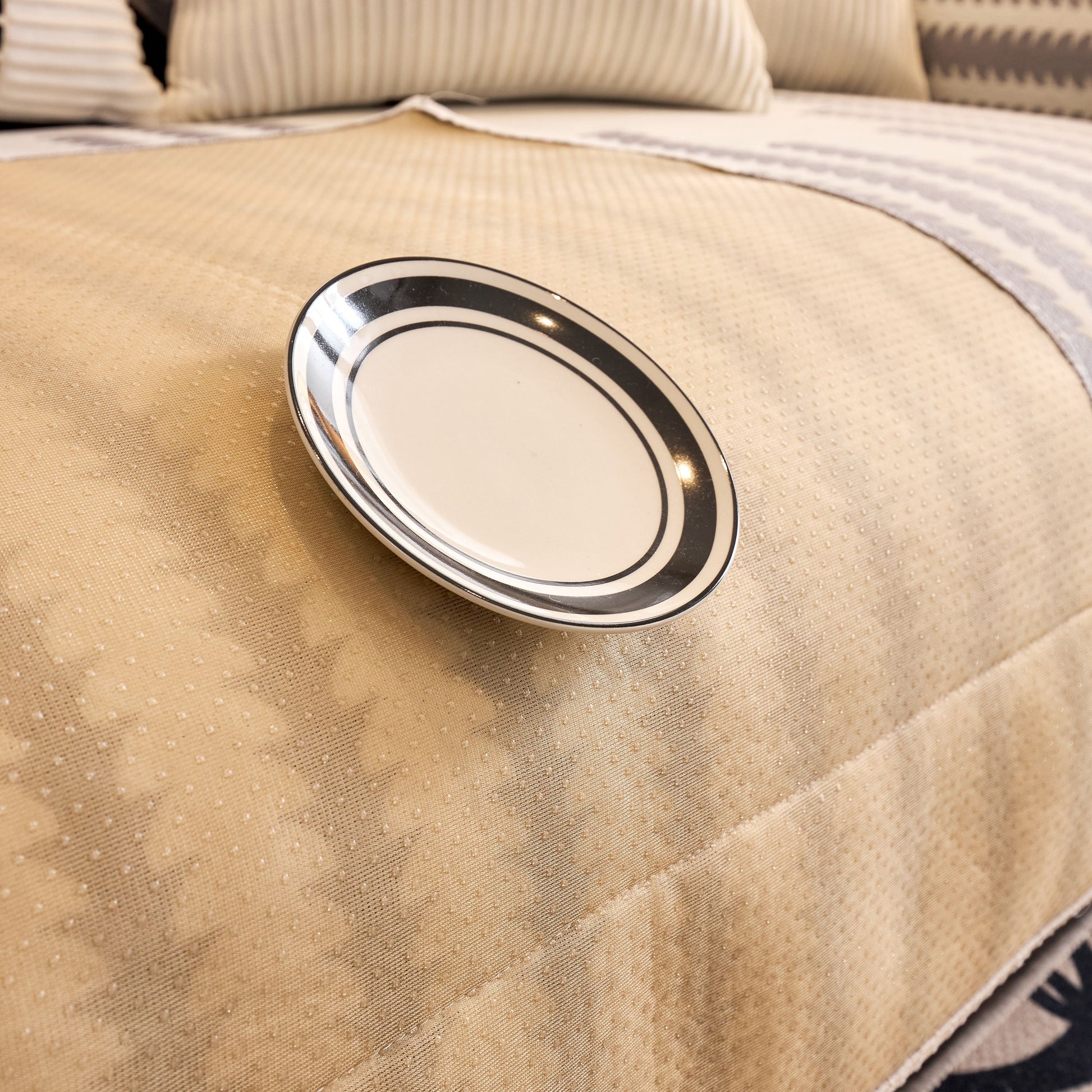 Decorative plate on patterned beige surface with pillows in background