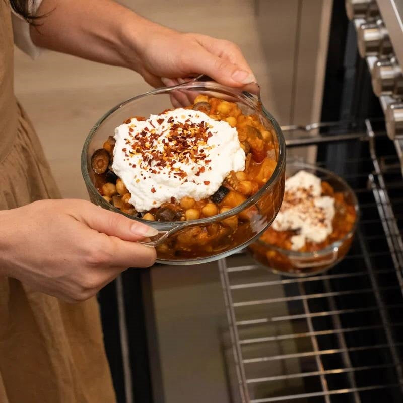 Woman removing Set of 2 - 1-Quart Glass Dutch Oven Casserole Bakeware Baking Dishes with Lids from oven, filled with cooked meal.