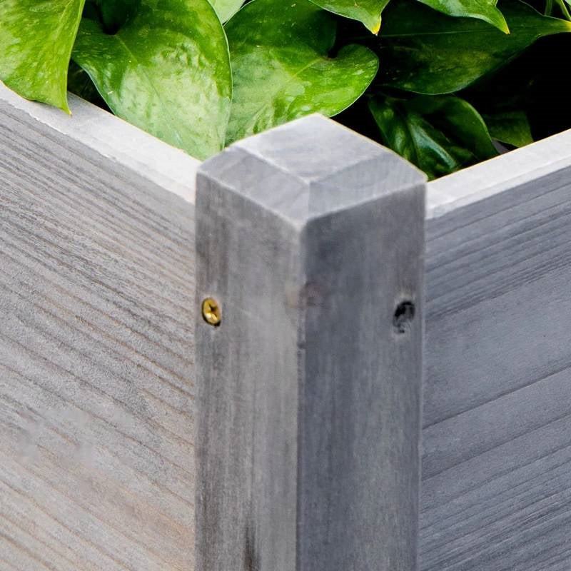 Close-up of a corner of the 3 Grey Wood Elevated Planter Set Vegetable Herb Flowers Raised Garden Beds with leafy greens.