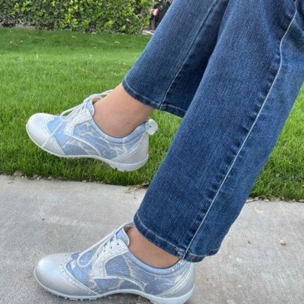 Person wearing WesTees Grace shoes with abstract blue and silver print lace, on grass background