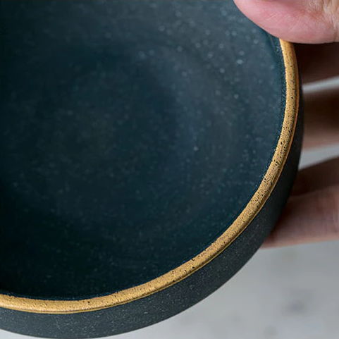Close-up of Galileo Tableware matte green plate with golden ring detail, handcrafted porcelain, elegant dining accessory.