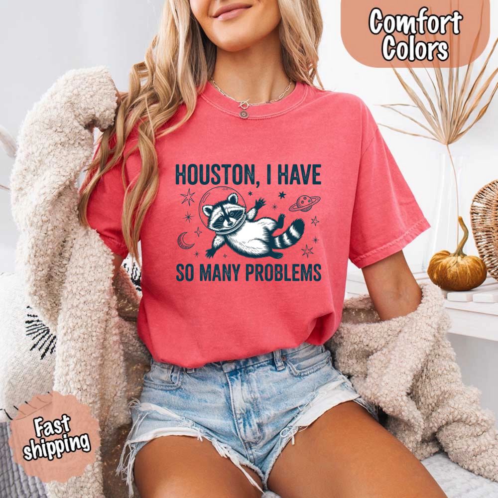 Woman wearing Houston I Have So Many Problems Raccoon Comfort Colors T-Shirts with a space raccoon graphic, fast shipping available.
